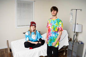 ale and Female Patients in Happy Cloud Adaptive Clothing, Female Wearing Happy Cloud Beanie, Both Smiling on Hospital Bed