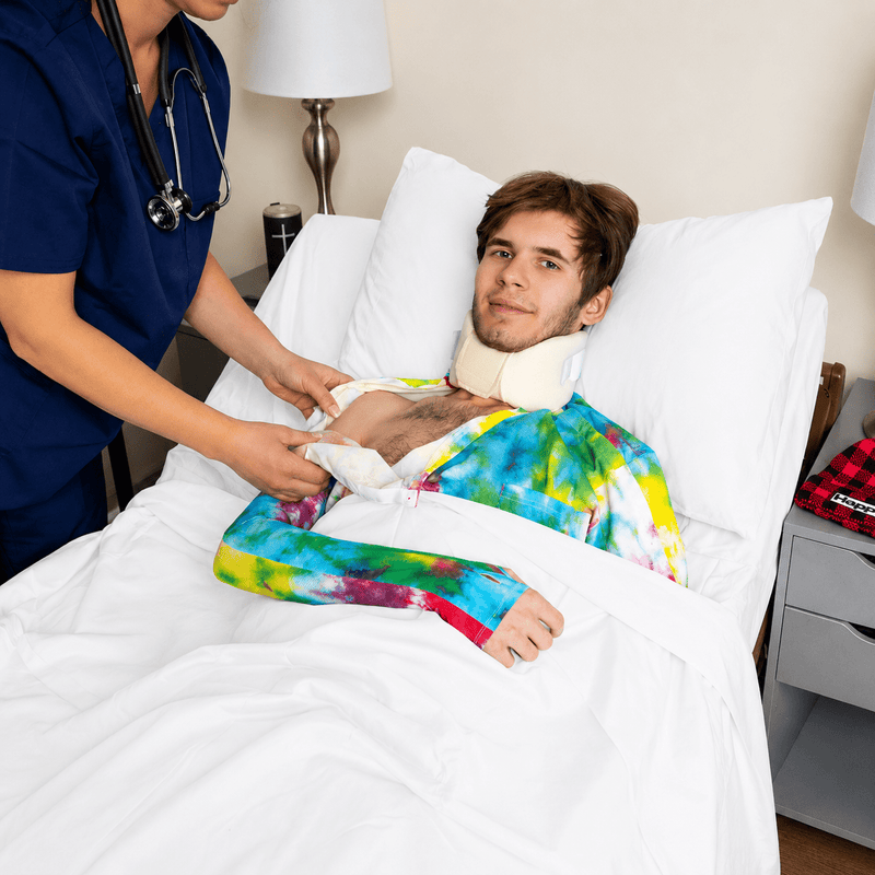 Man in a hospital bed with a neck brace, attended by a healthcare professional.