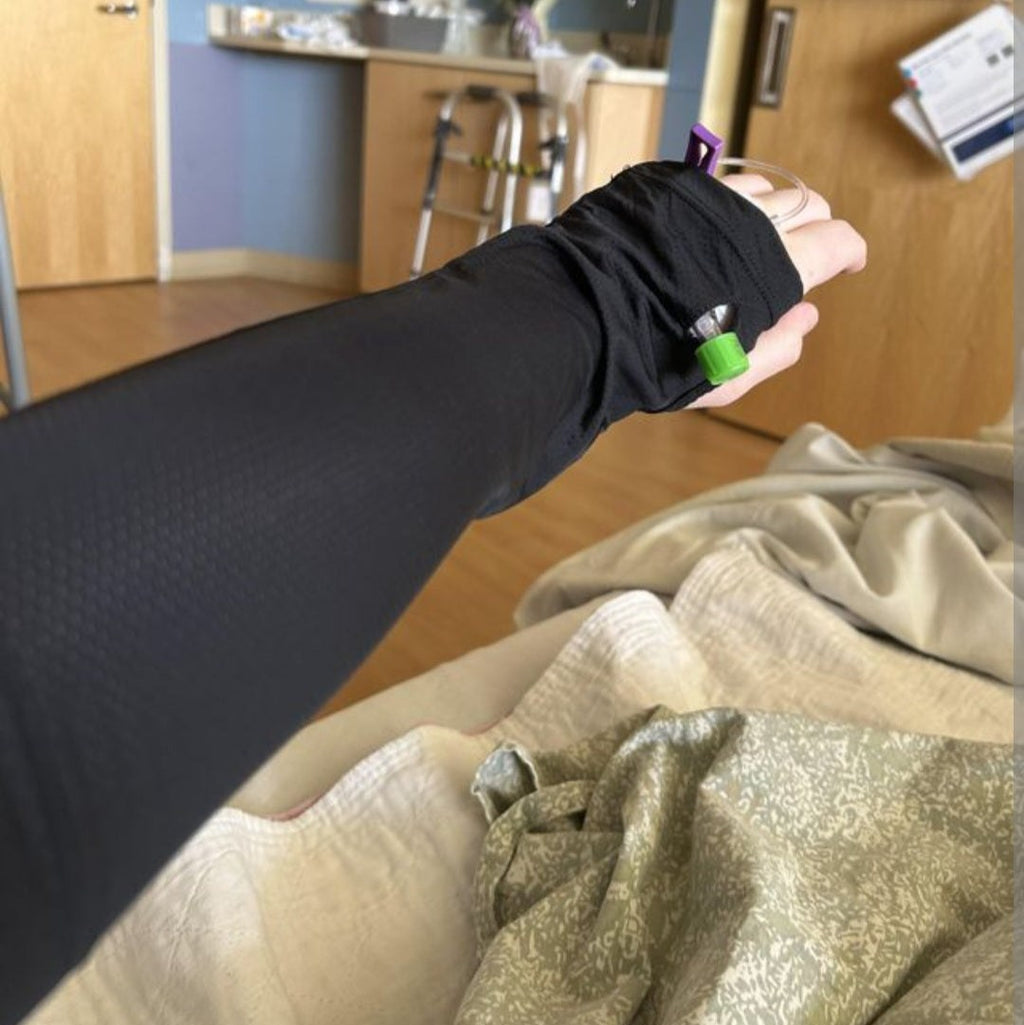 Person wearing black adaptive port access sleeve with medical tubing in a hospital or recovery setting